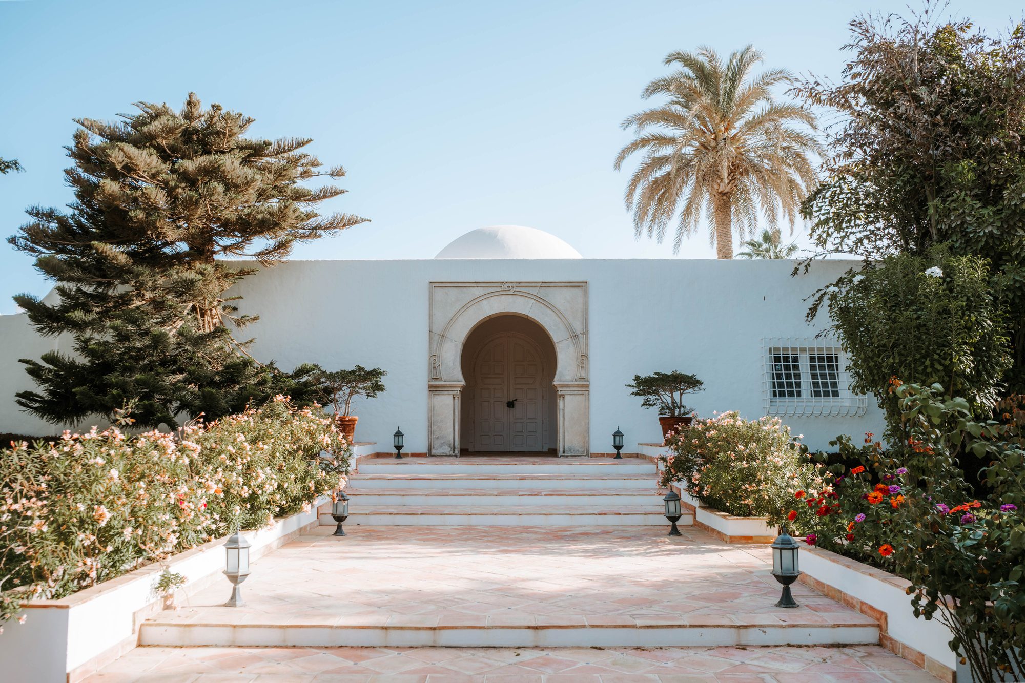 A white Moorish-arched villa entrance in Dakar, framed by palms and flowering vines