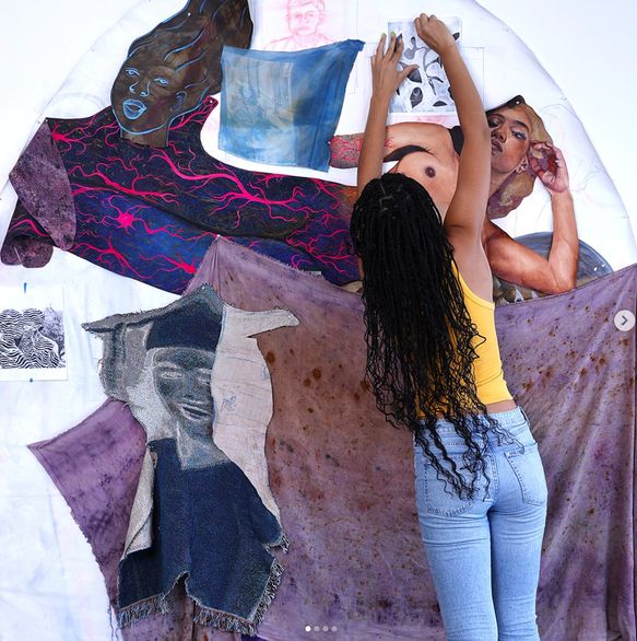 An artist assembling a mixed-media textile and portrait installation